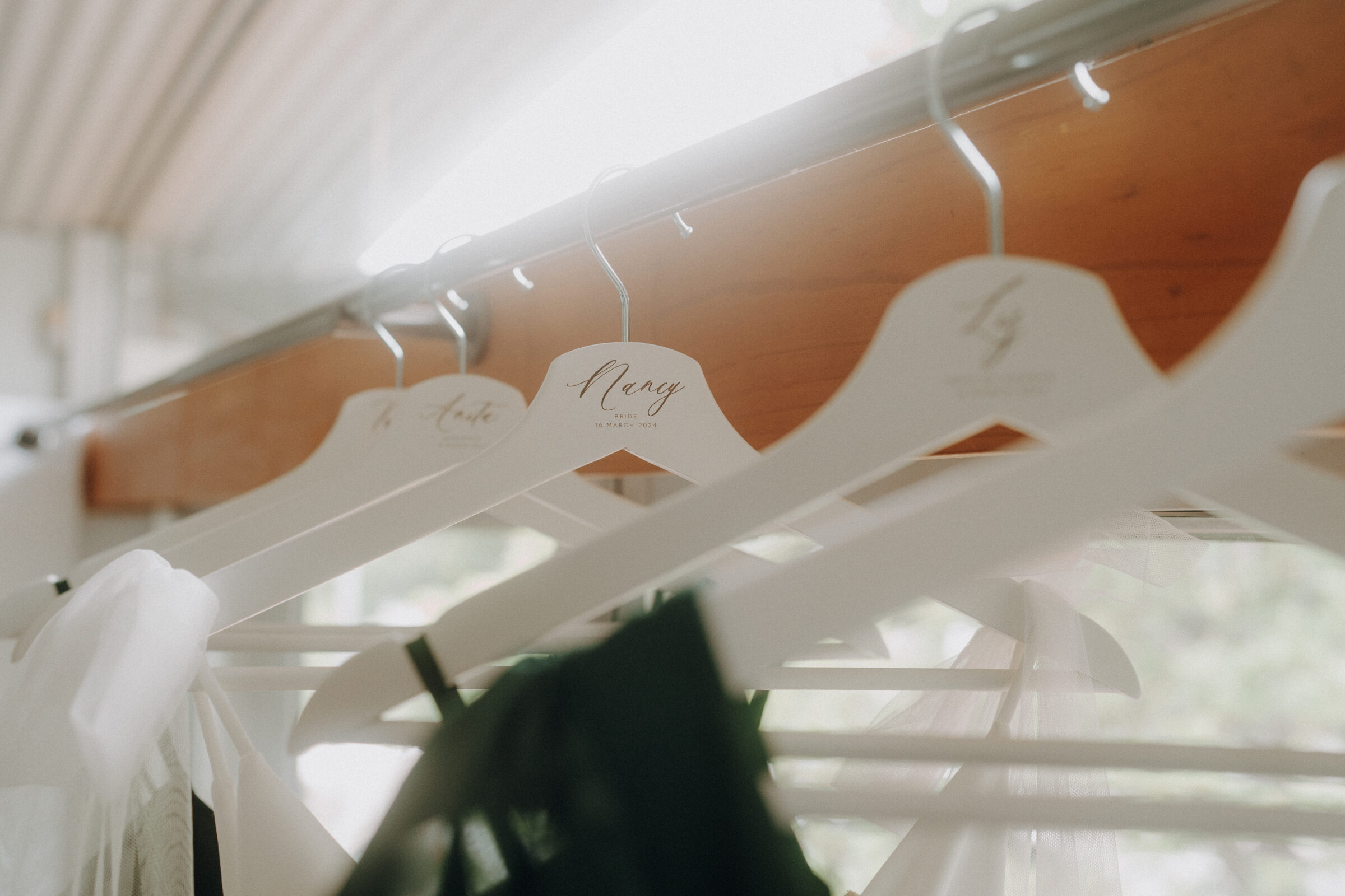 Clothes hang on personalized white hangers in a bright room, with names and logos visible.