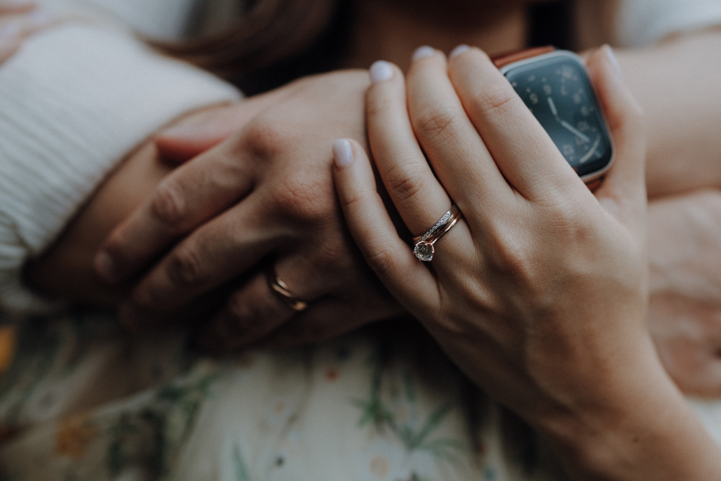 Close-up of a couple's hands intertwined, showing rings on their fingers. One person wears a watch.