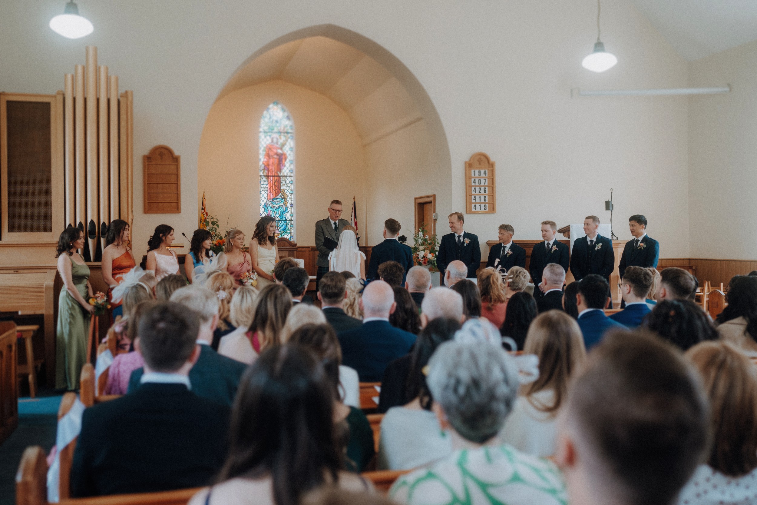 A wedding ceremony taking place in a church, with a couple standing before an officiant at the altar, wedding party members nearby, and guests seated in pews.