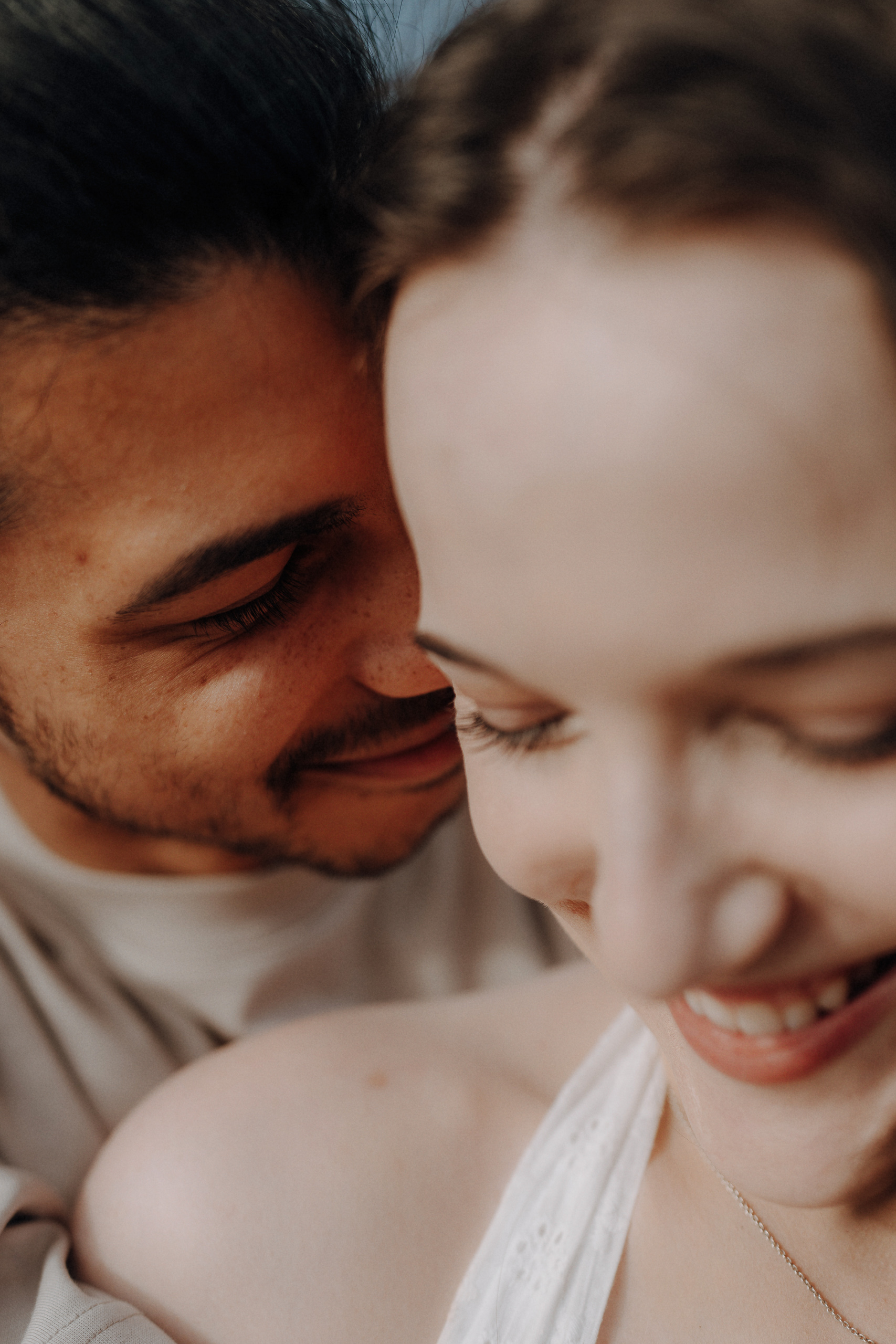A close-up of two people smiling, with one person leaning in towards the other’s face, both appearing happy and relaxed.